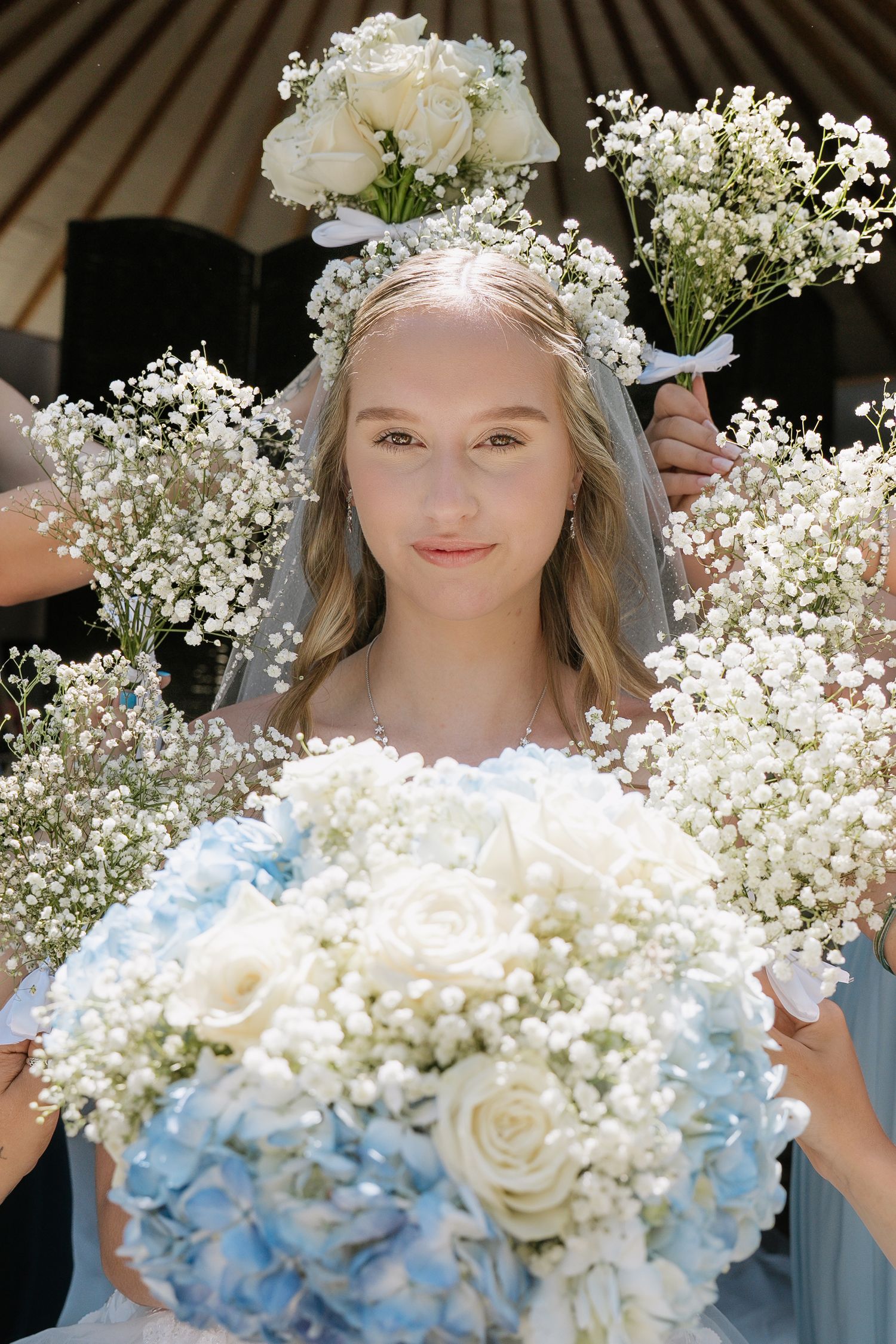 A dreamy bridal portrait featuring delicate baby's breath crown and a bouquet of white roses with blue hydrangeas.