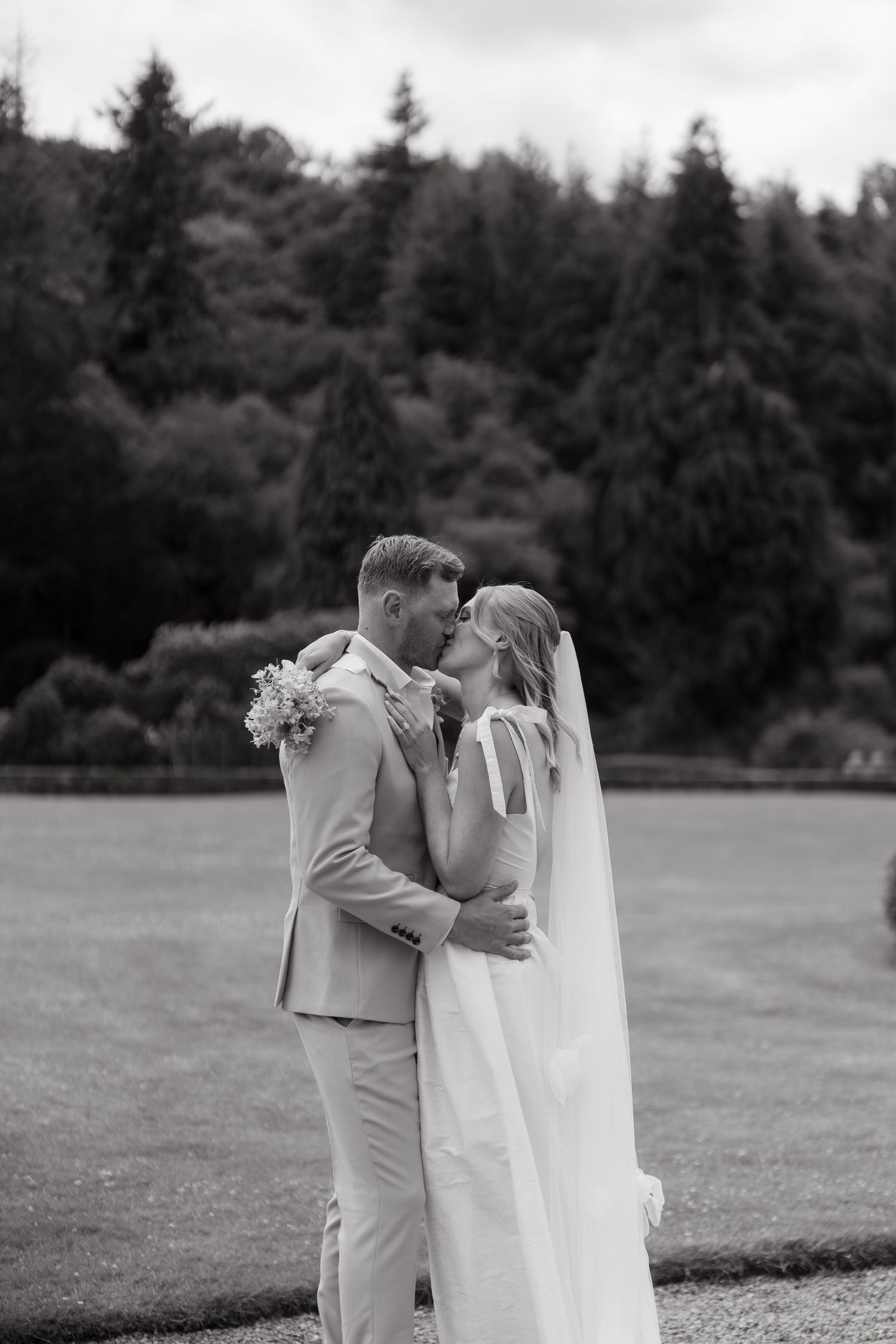 A flowing white veil billows gracefully in the wind across a grassy field in black and white photography.
