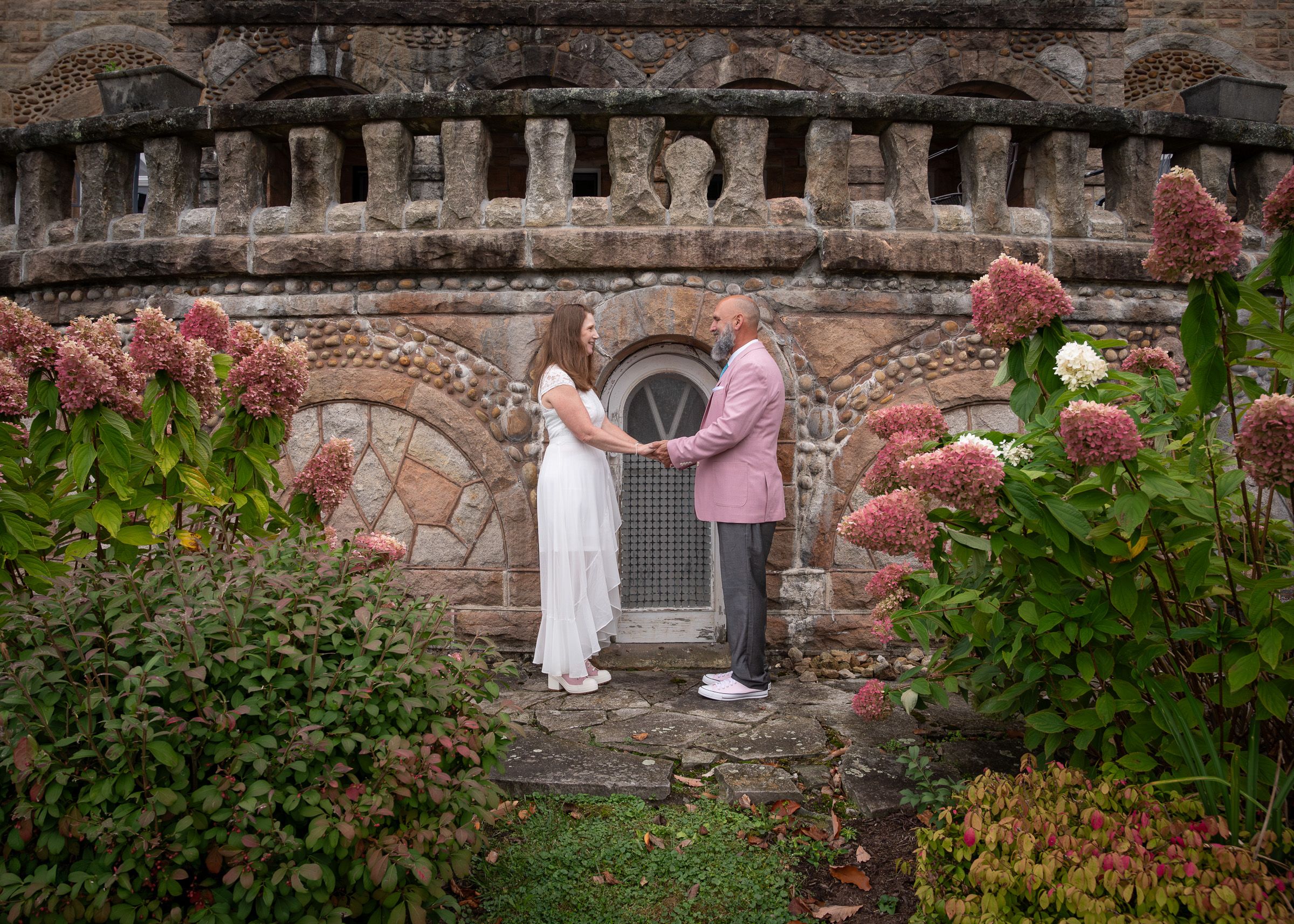 Historic stone wall with decorative balustrade surrounded by blooming flowers at dusk.