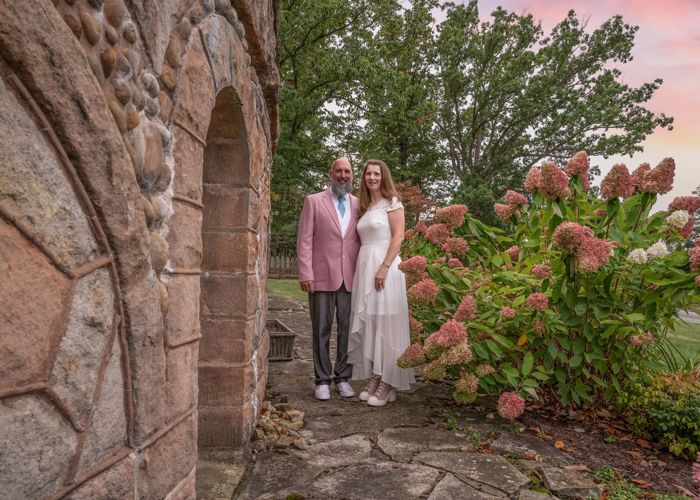 Stone archway in a garden setting during sunset with pink sky.