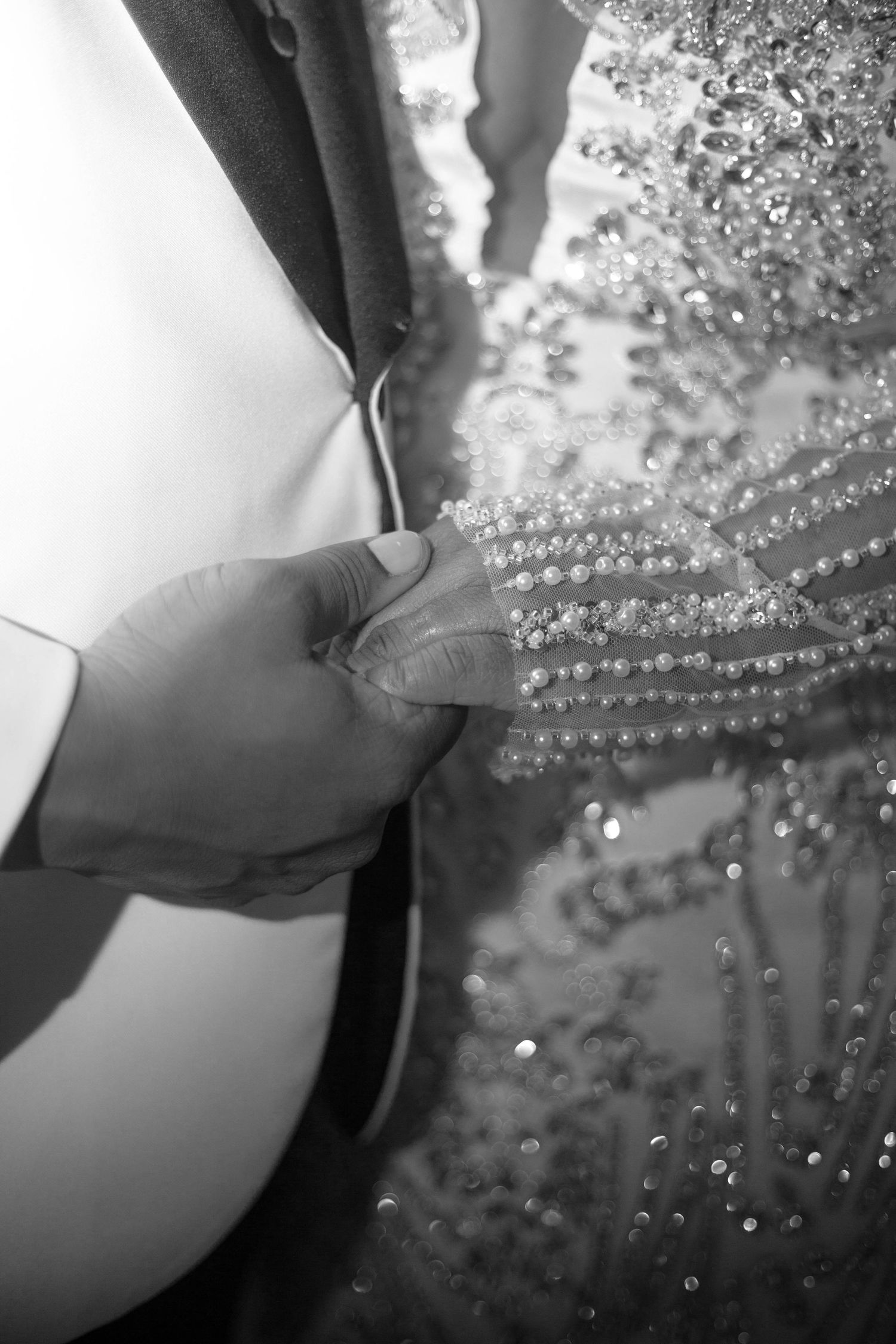 Black and white close-up of hands adjusting delicate beaded details on elegant formal attire.