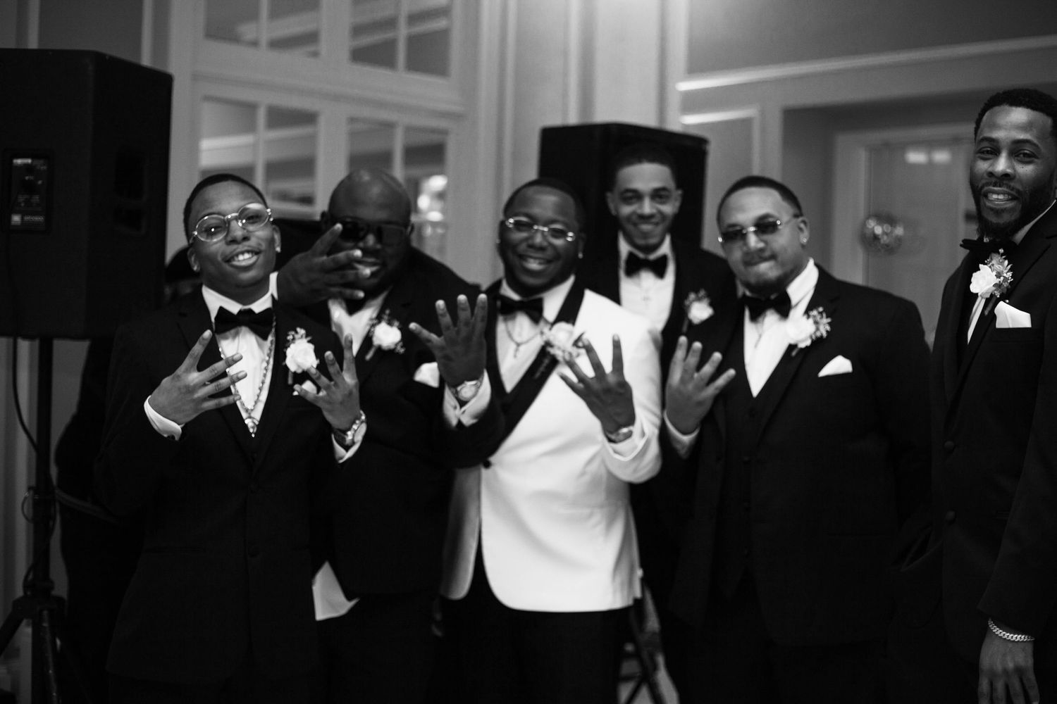 A group of people in formal attire laugh and smile together during what appears to be a wedding celebration.