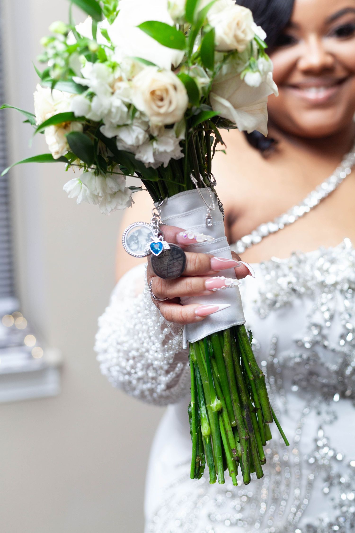 Close-up of elegant white rose bridal bouquet with crystal-adorned dress details in soft focus background.