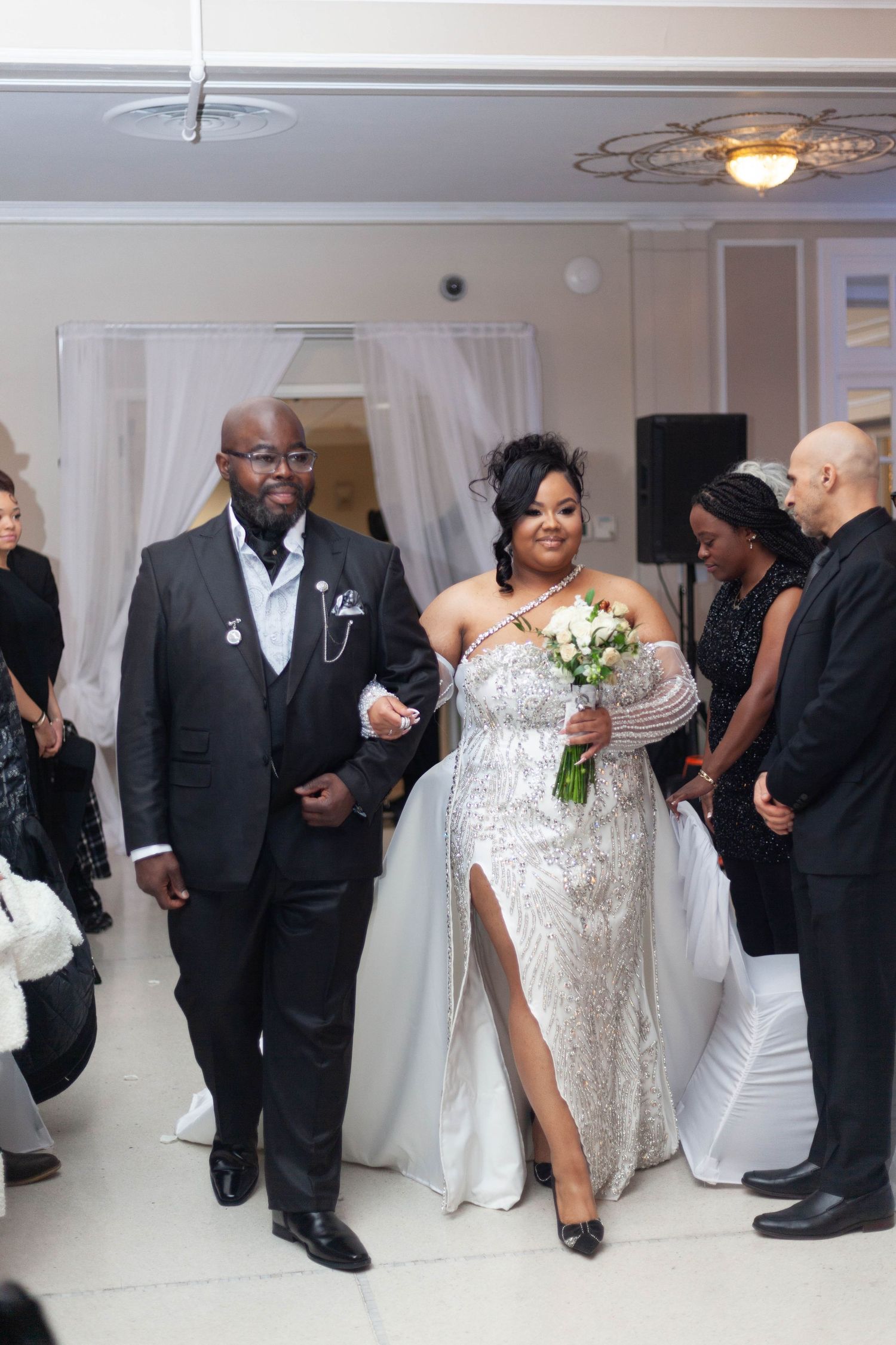 Wedding celebration in a white-decorated venue with guests in formal attire gathered for festivities.