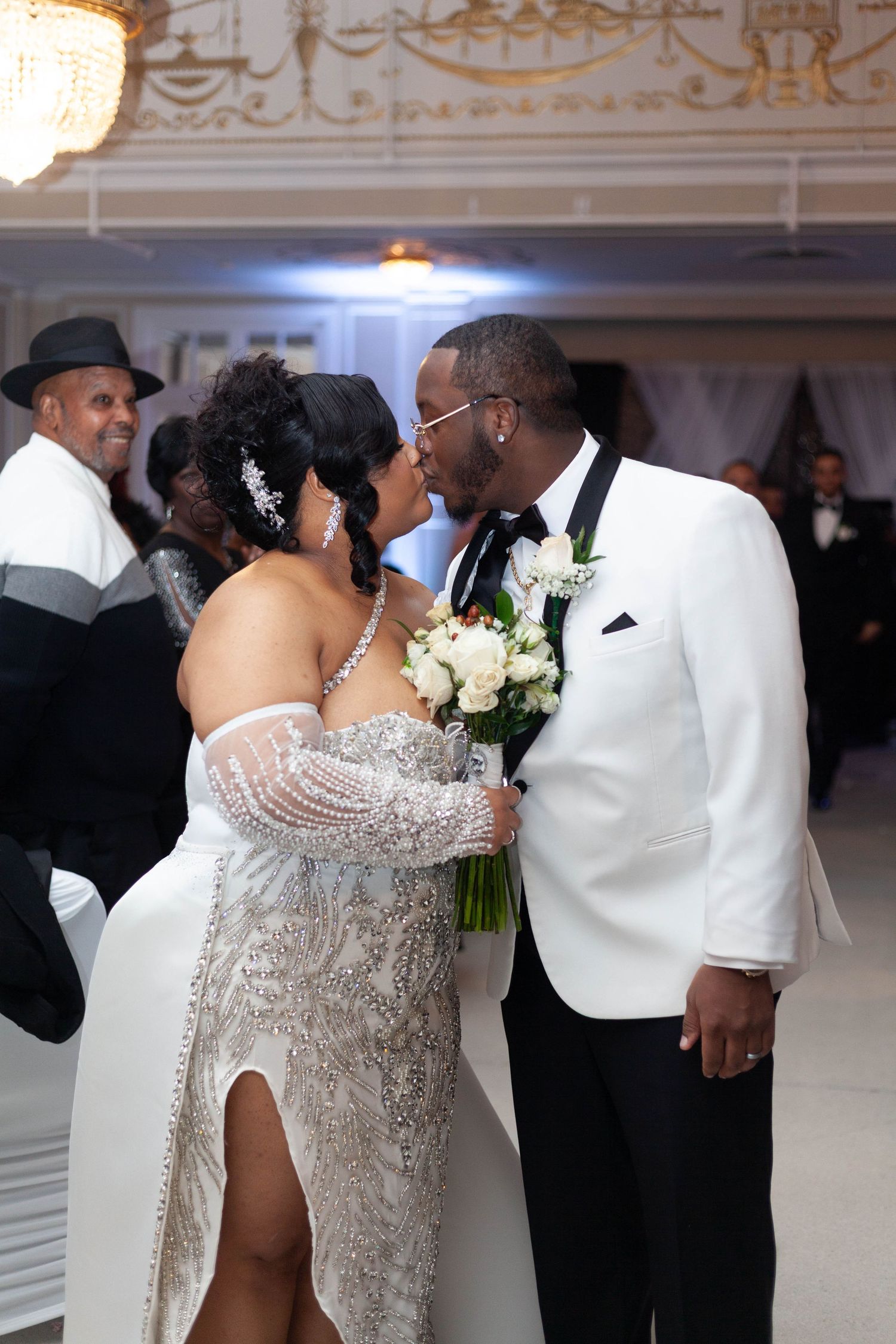 Elegant wedding reception scene with couples dancing in formal attire including white tuxedos and sparkly gowns.