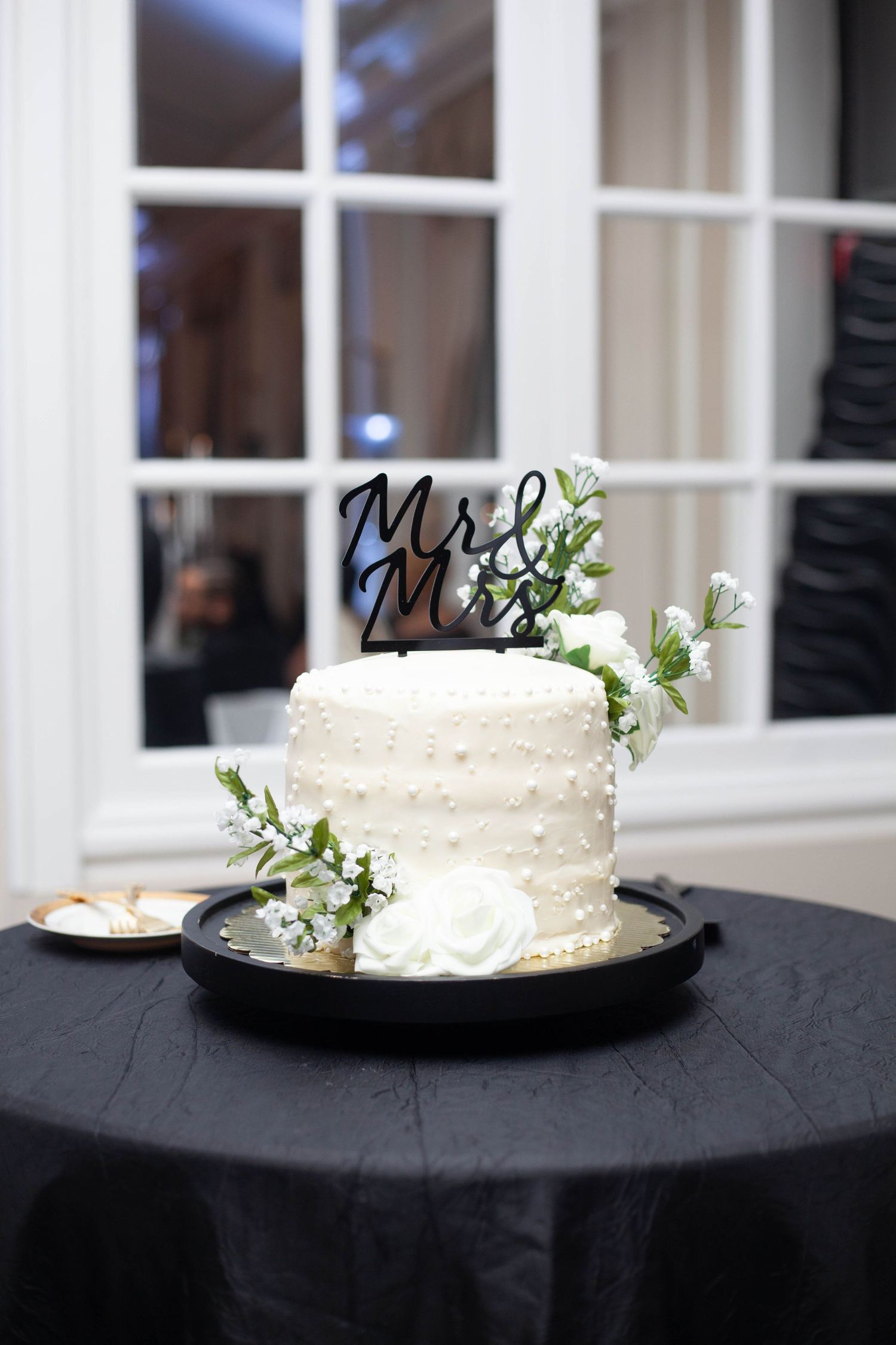 A row of small white wedding cakes decorated with delicate floral accents on black plates against a light background.