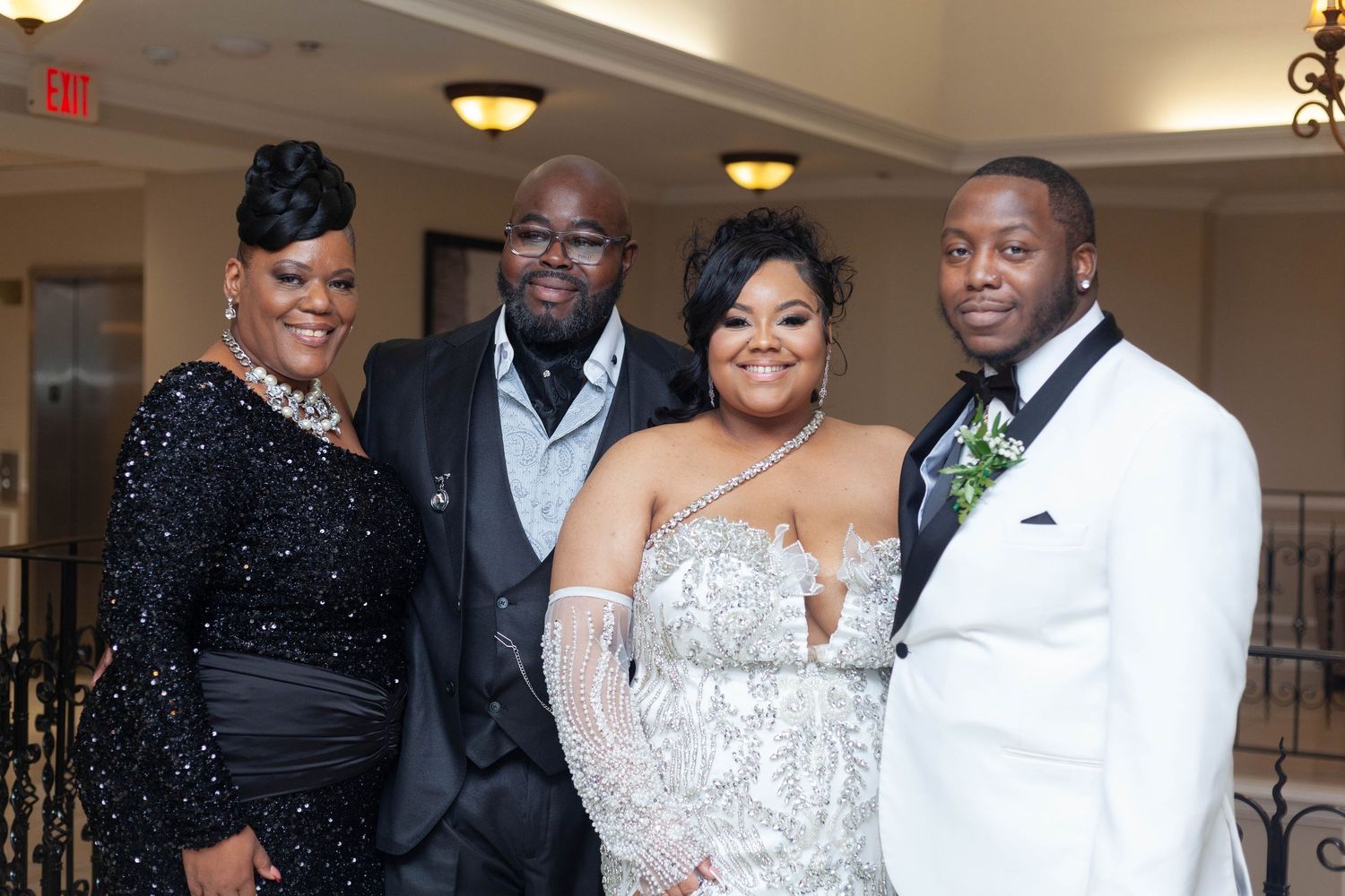 A wedding celebration with guests in formal attire including black suits and sparkly dresses dancing and posing together.