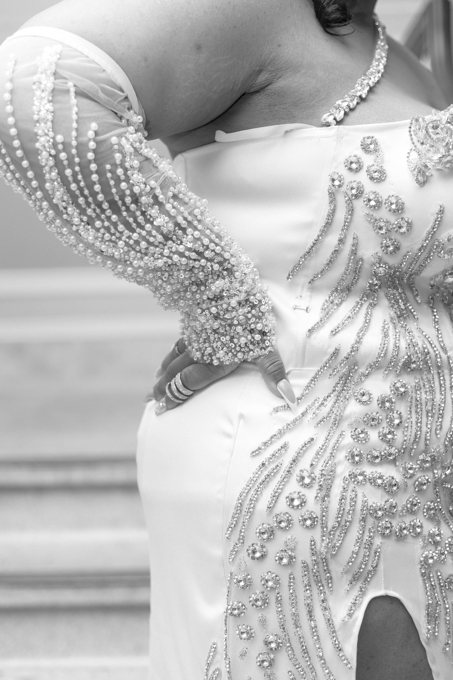 Close-up detail of an elegant white wedding dress with intricate crystal beading in a feather-like pattern.