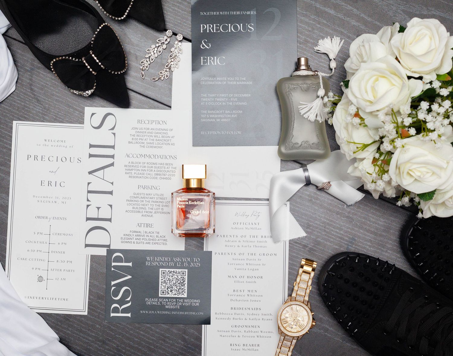 Wedding details flatlay with invitations, perfume, watch, and white flowers on a dark gray surface.