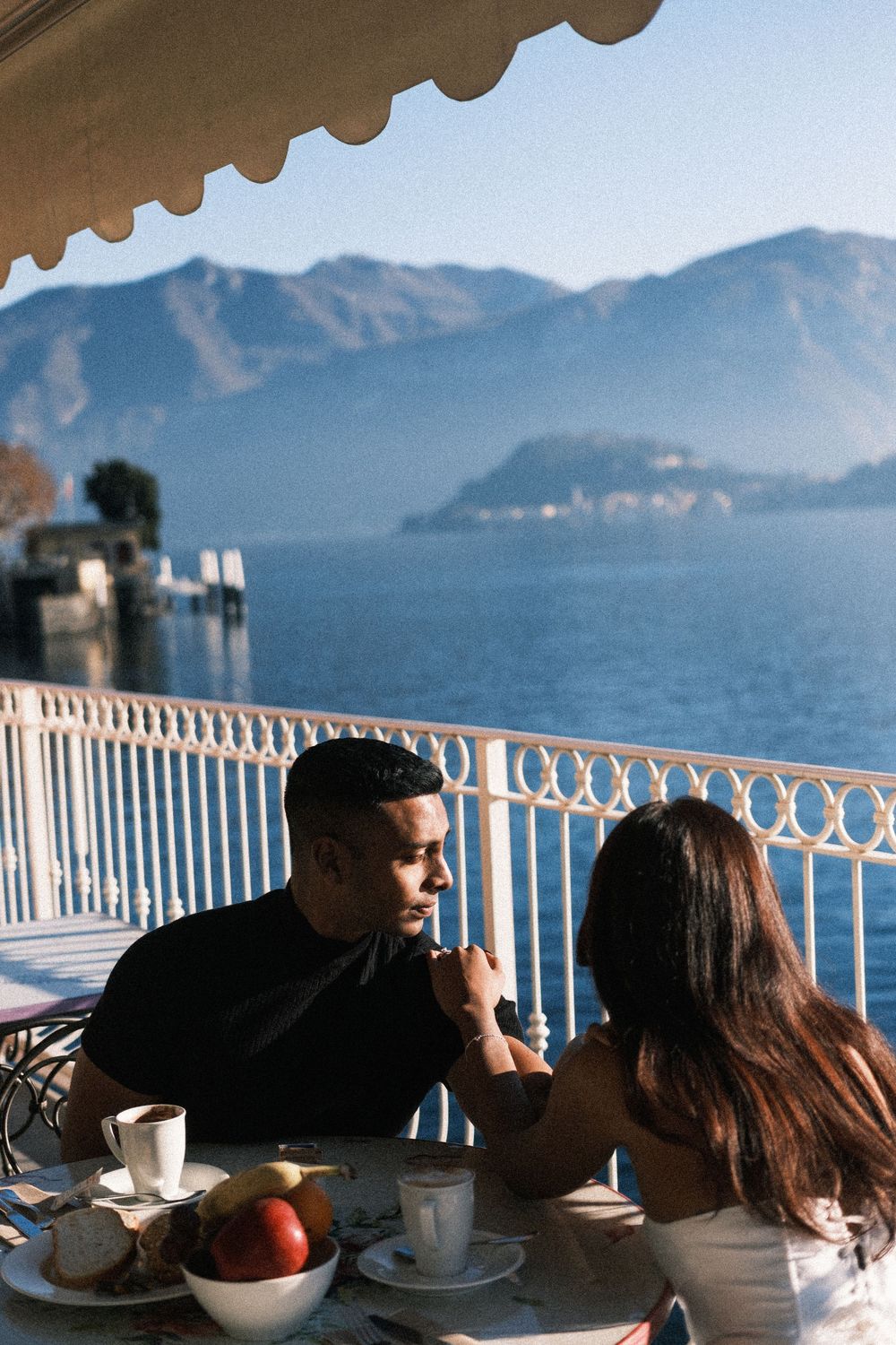 Couple enjoying coffee and conversation at an outdoor cafe overlooking a scenic mountain lake view.