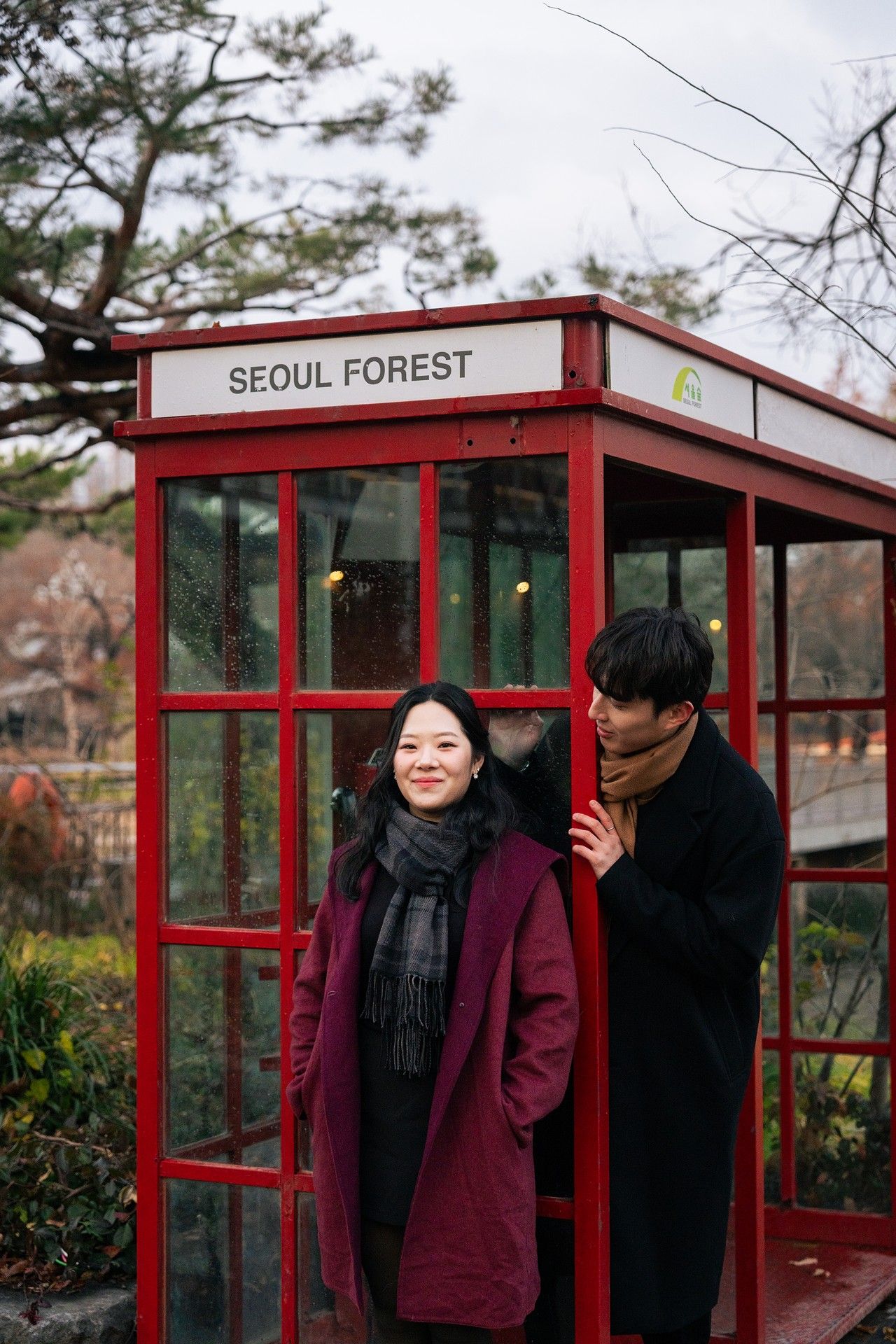 A red phone booth labeled 'Seoul Forest' with two people standing together in winter attire.