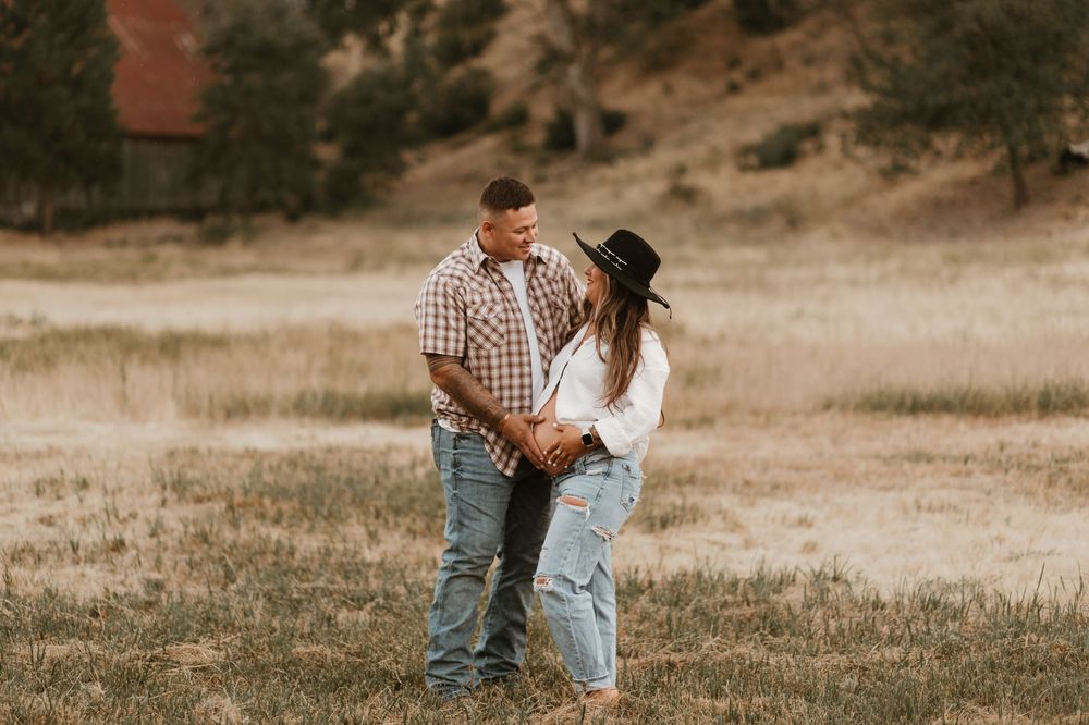 A couple in casual attire walks together through a golden field during sunset in a romantic outdoor setting.