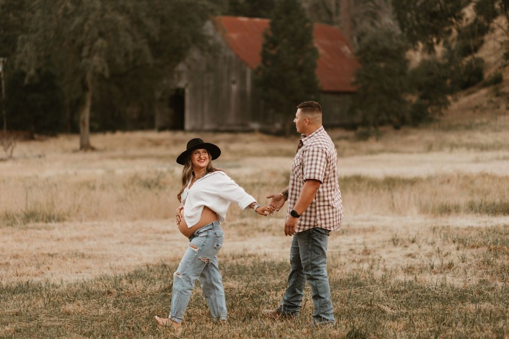 A couple dances together in a grassy field during golden hour at sunset.
