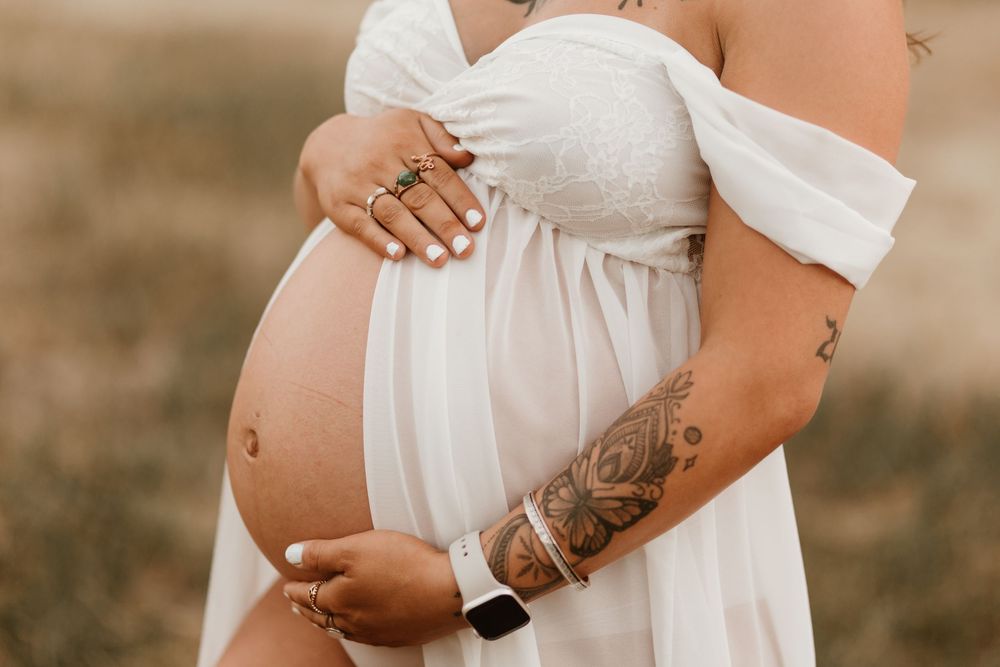 Close-up maternity photos showing a pregnant woman's belly in a flowing white dress against a warm outdoor background.