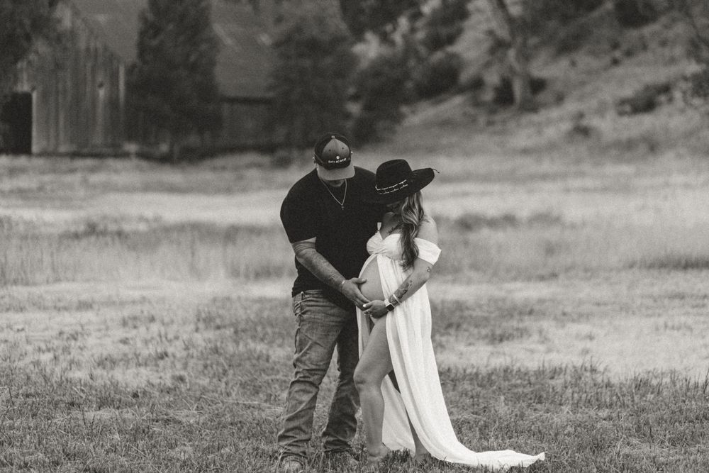 A couple embraces in a grassy meadow during a black and white photoshoot.