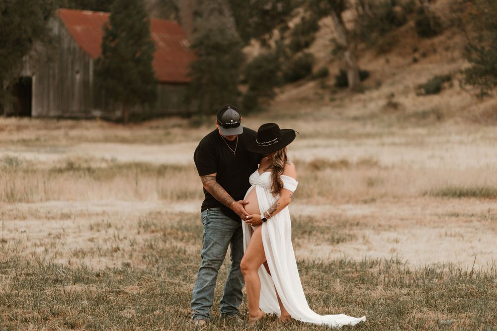 A couple embraces in a romantic moment on a rustic field during golden hour.