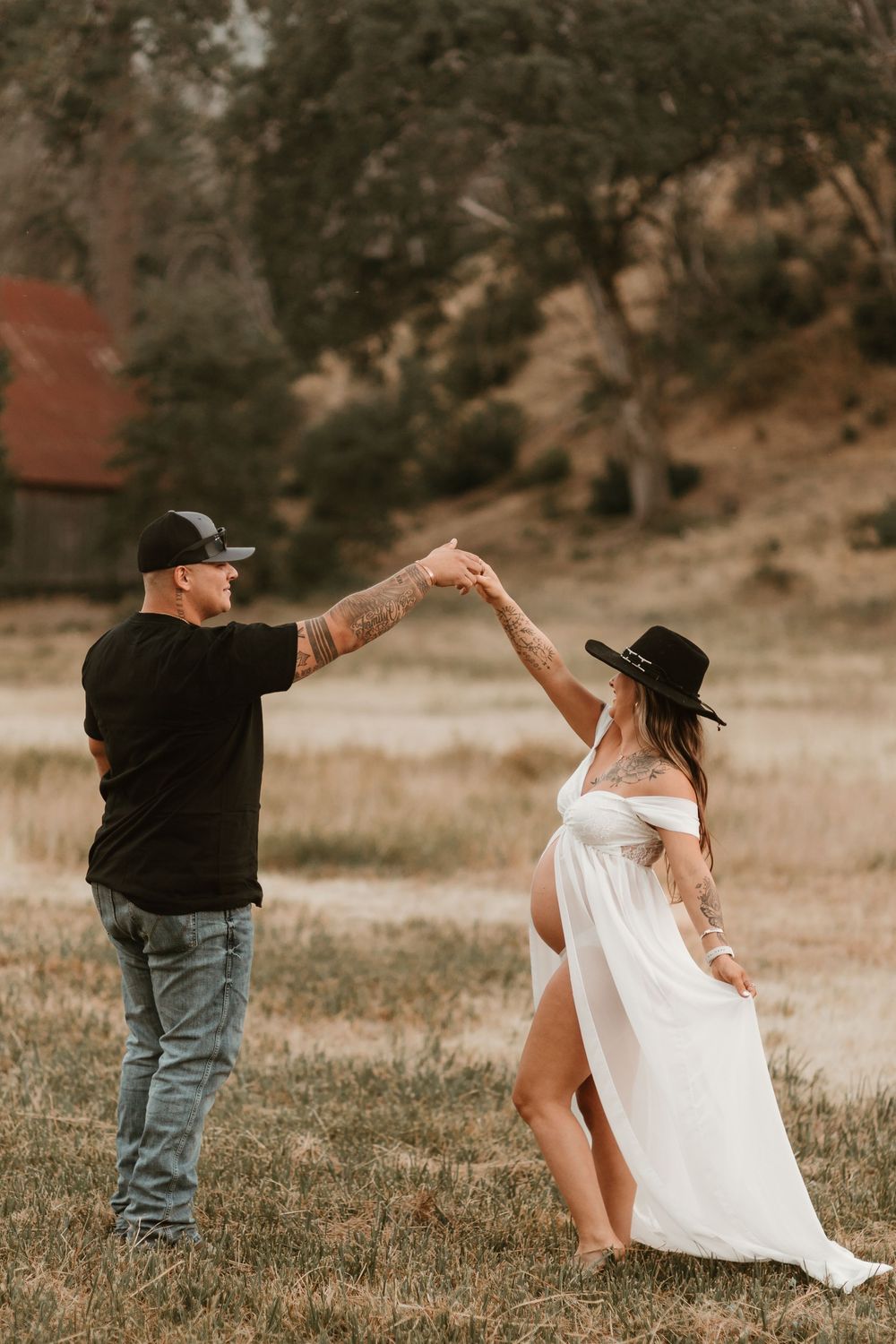 A couple in a field dancing together at sunset, with her in a flowing white dress and him in casual attire.