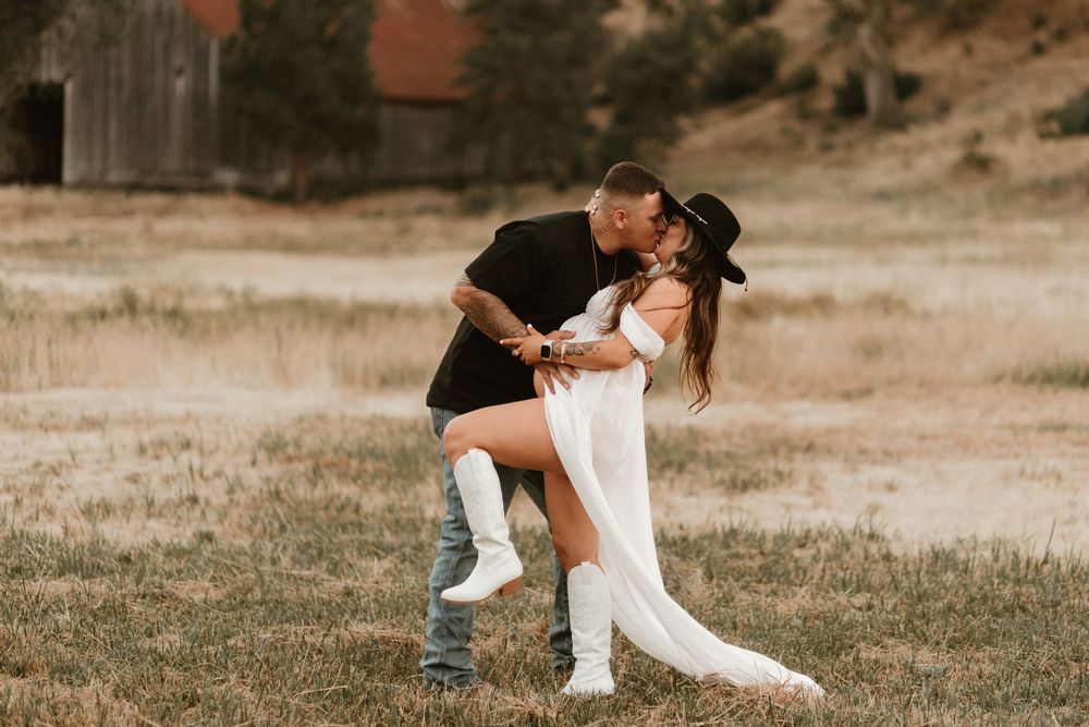 Romantic outdoor couple's photoshoot with white dress and casual attire in a rustic field setting.