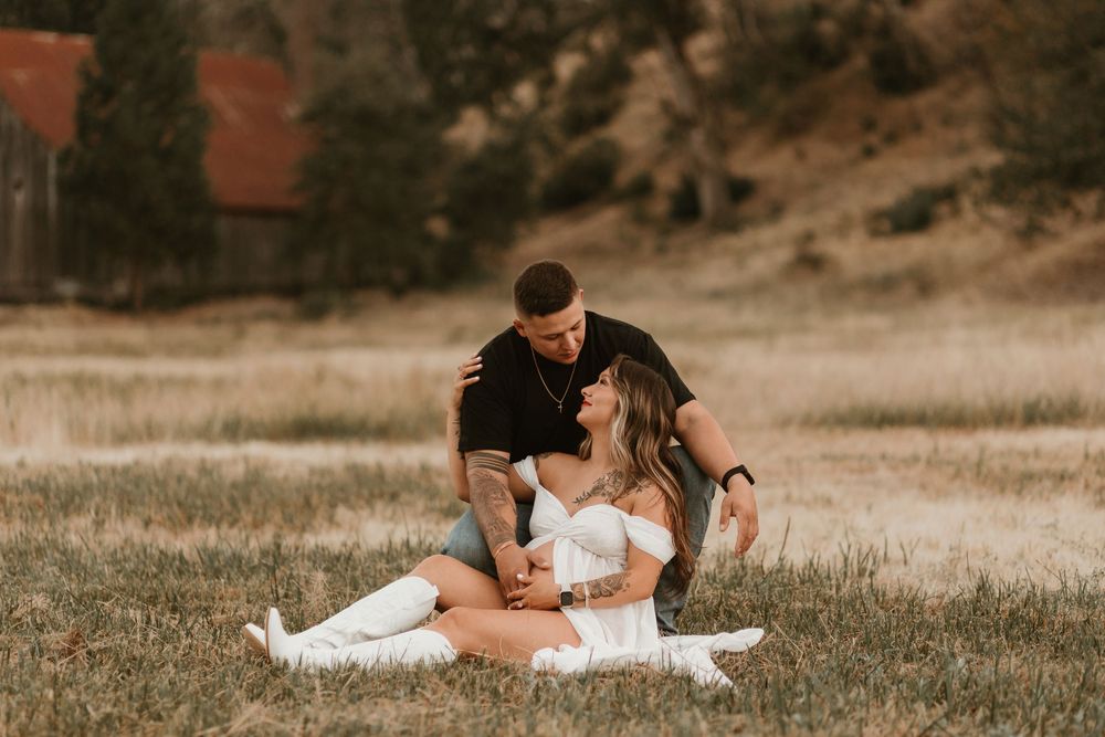 A couple sits together on a grassy field during a warm sunset engagement photo session.