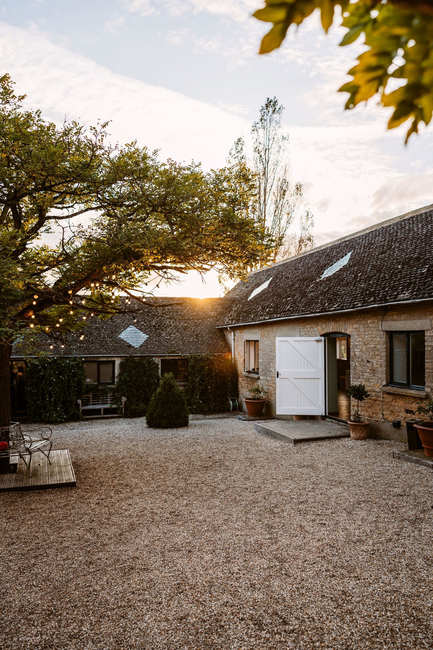 Stone and white ranch-style house exterior with gravel driveway at sunset, framed by autumn leaves.