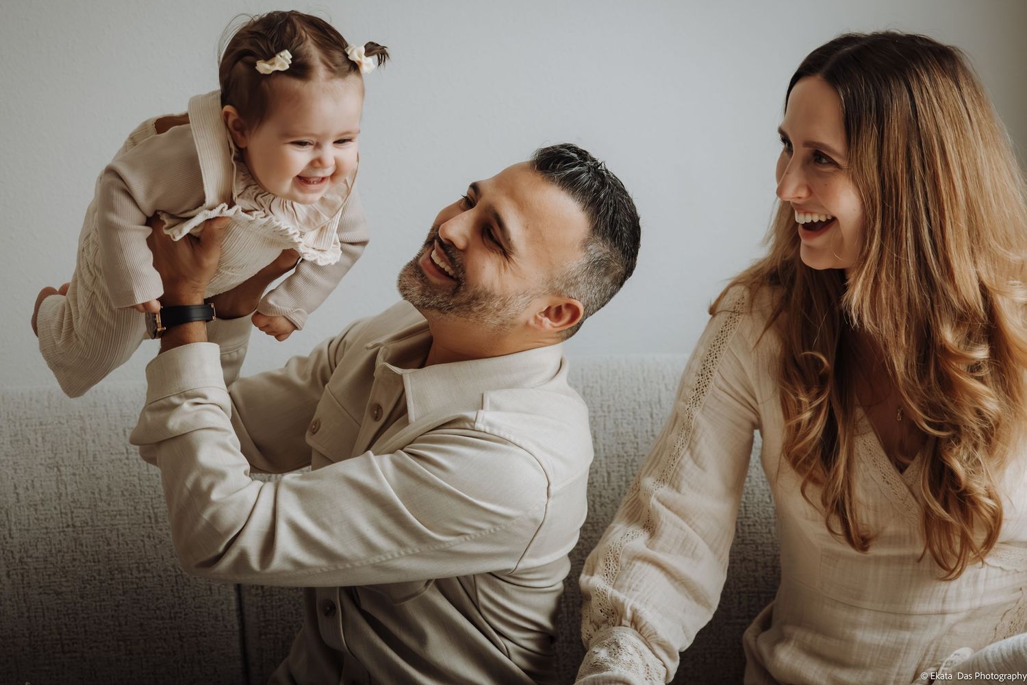 A family in white clothing shares tender moments while playing together indoors.