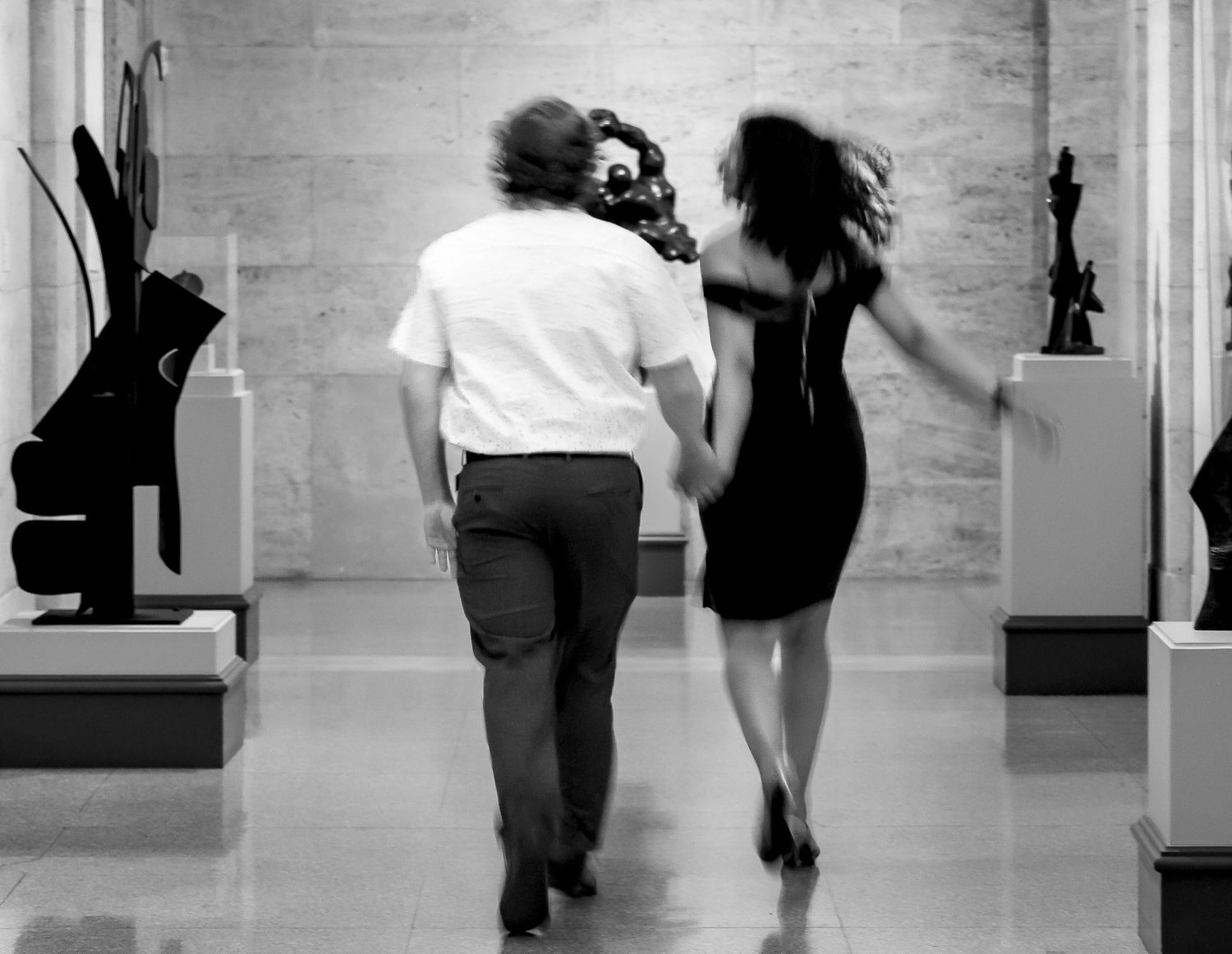 People in silhouette dance and move in front of a white brick wall in an art gallery space.