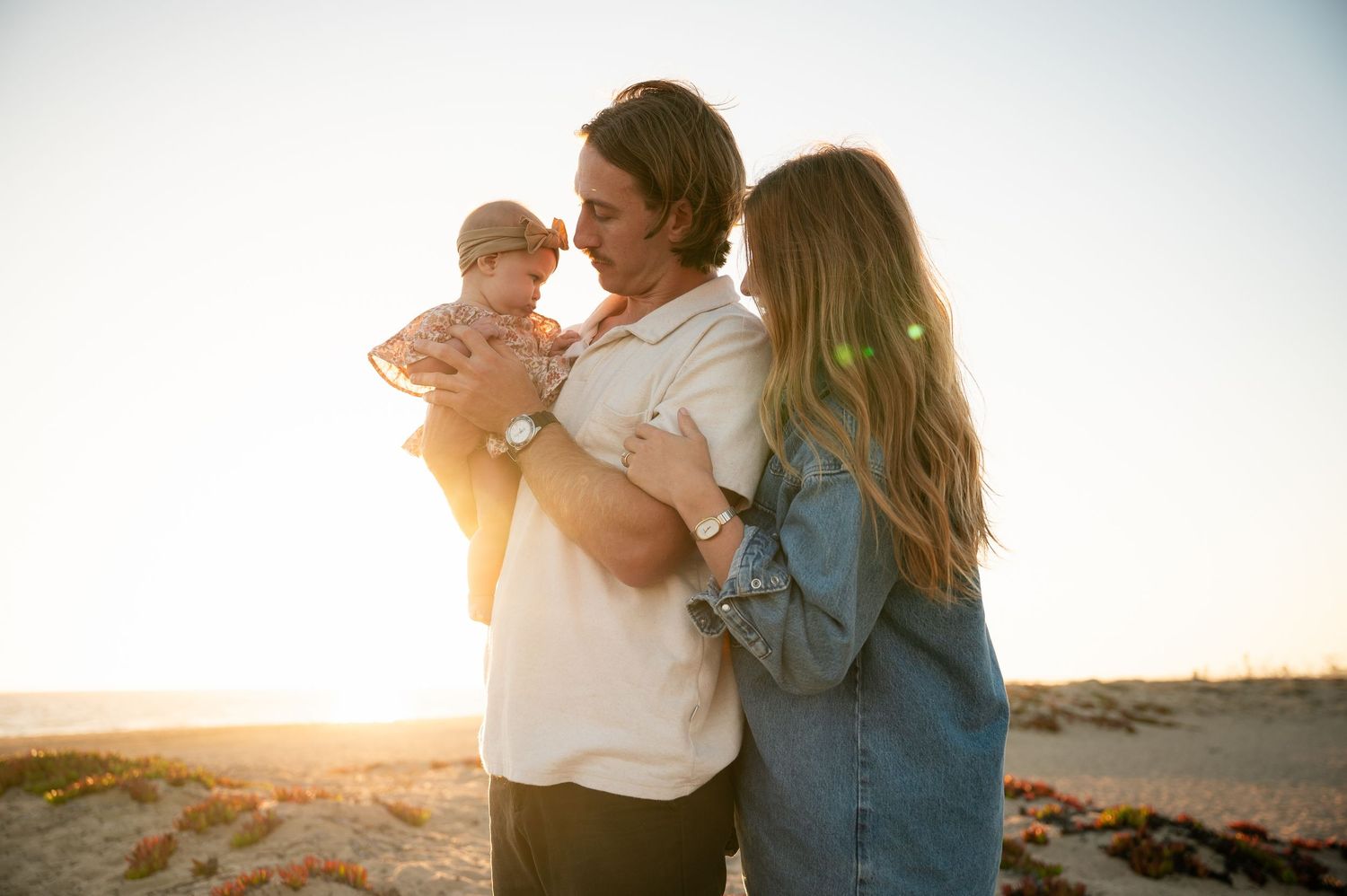 A couple embraces on a beach at sunset with warm golden light illuminating the scene.