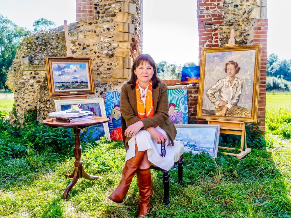 Editorial portrait of Gallerist Lucy Charles displaying paintings in a garden setting, Yoxford, Suffolk