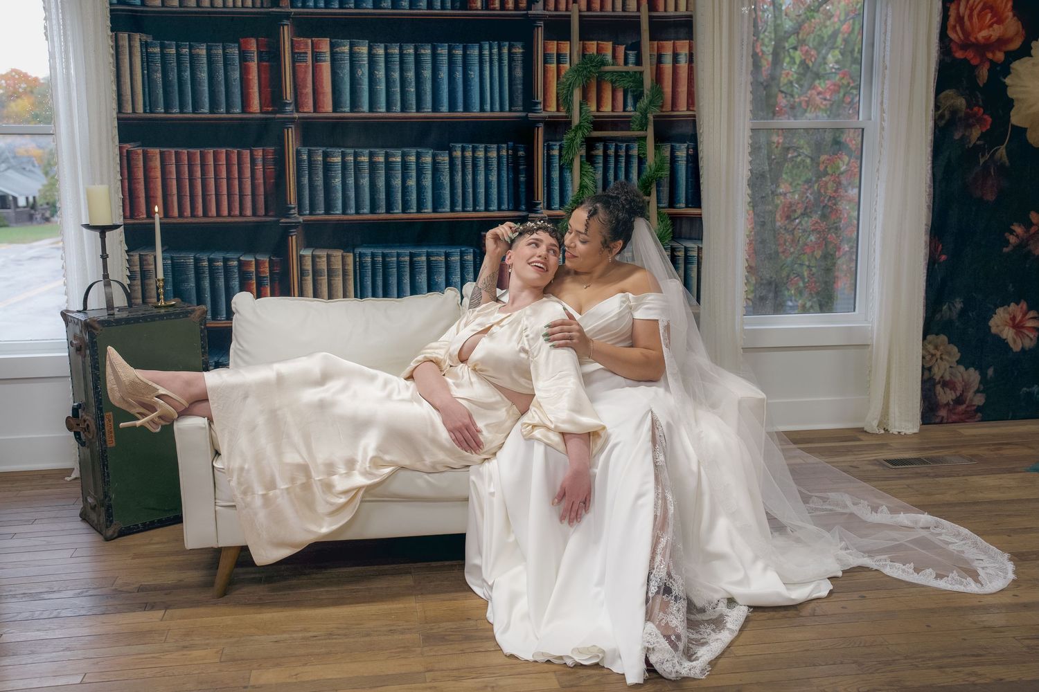 A figure in a flowing white wedding dress reclines elegantly across vintage furniture in a classic library setting.