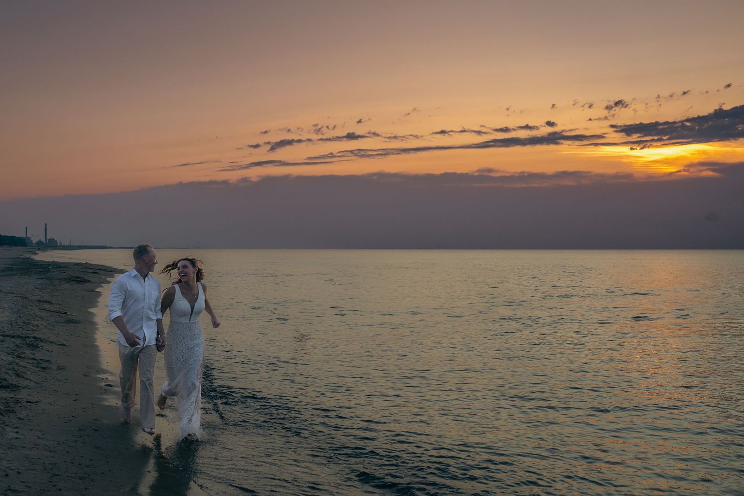 A couple walks along a beach at sunset with silhouettes against the golden sky and ocean backdrop.