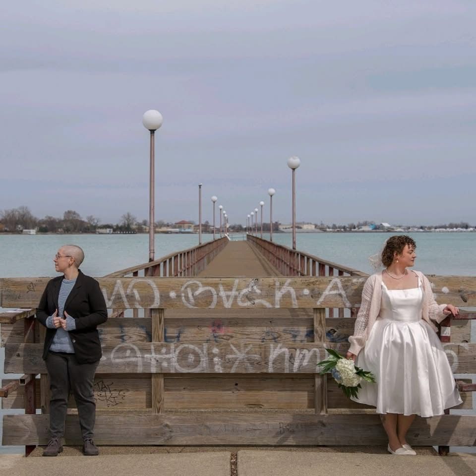 People sitting on a long pier or boardwalk by the water during an overcast day.