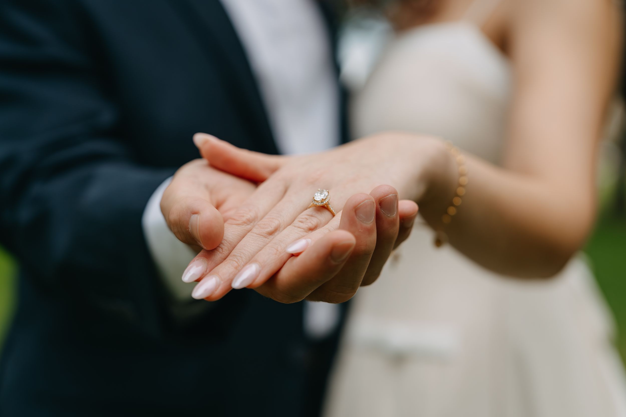 Bride and groom holding hands showing diamond engagement ring at wedding ceremony outdoors.