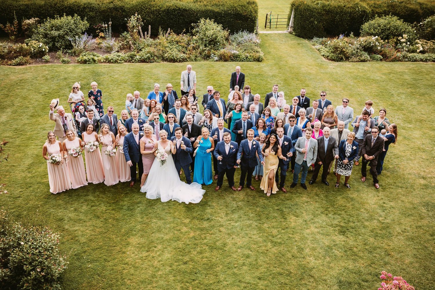 A group of wedding guests pose together on a lush green lawn at an outdoor celebration.