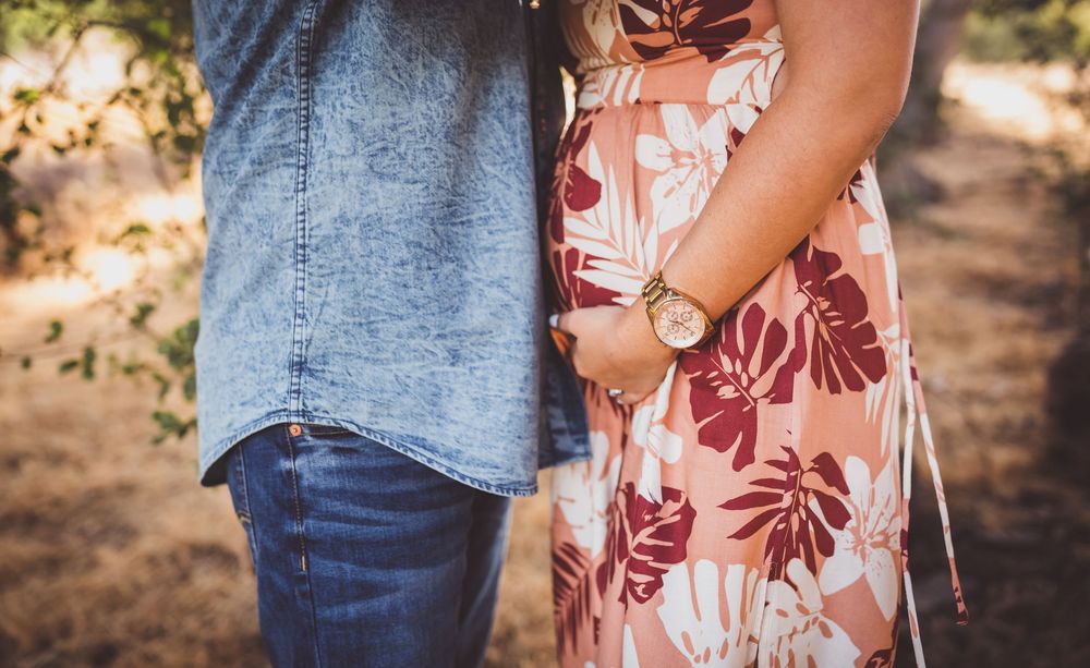 A couple in denim and floral attire hold hands while walking through a sunlit outdoor setting.
