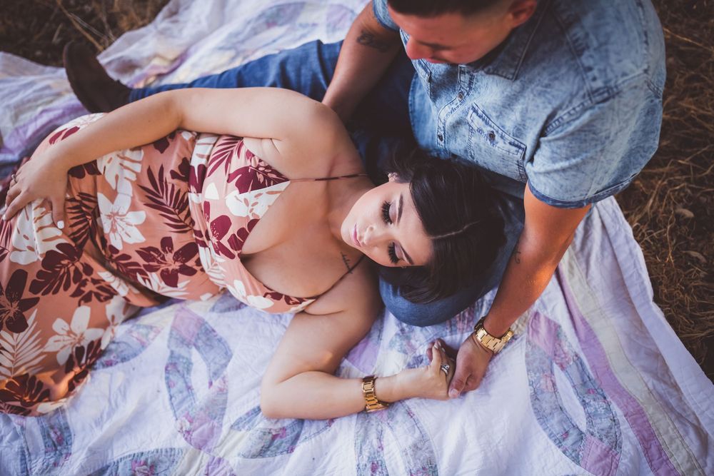 A couple in a romantic outdoor setting with a floral dress and denim outfit on a blanket.