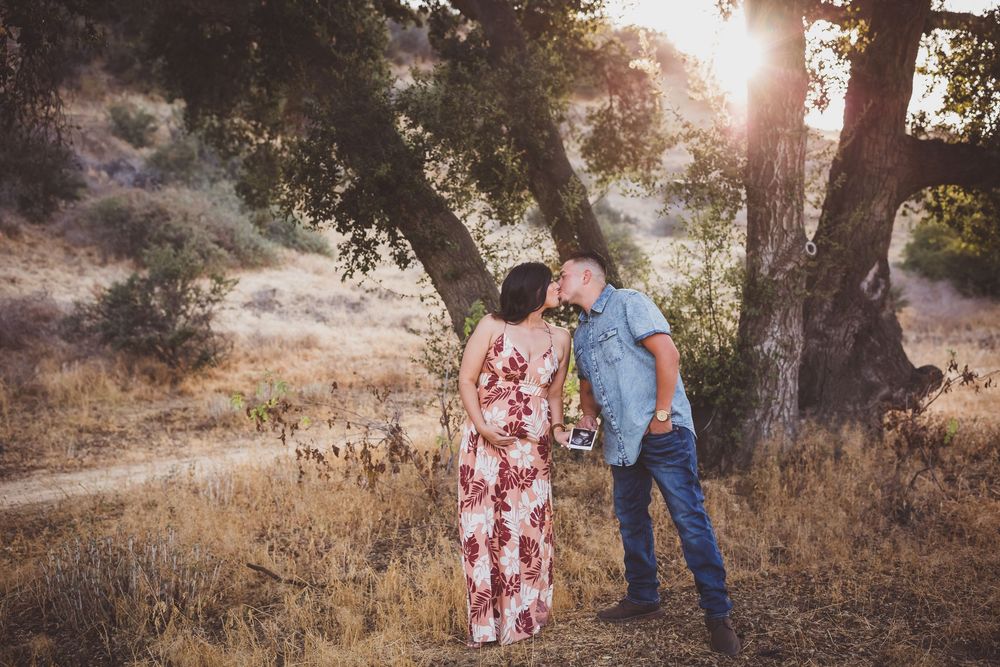 A tender moment captured between a couple in a natural setting with warm sunlight filtering through trees.
