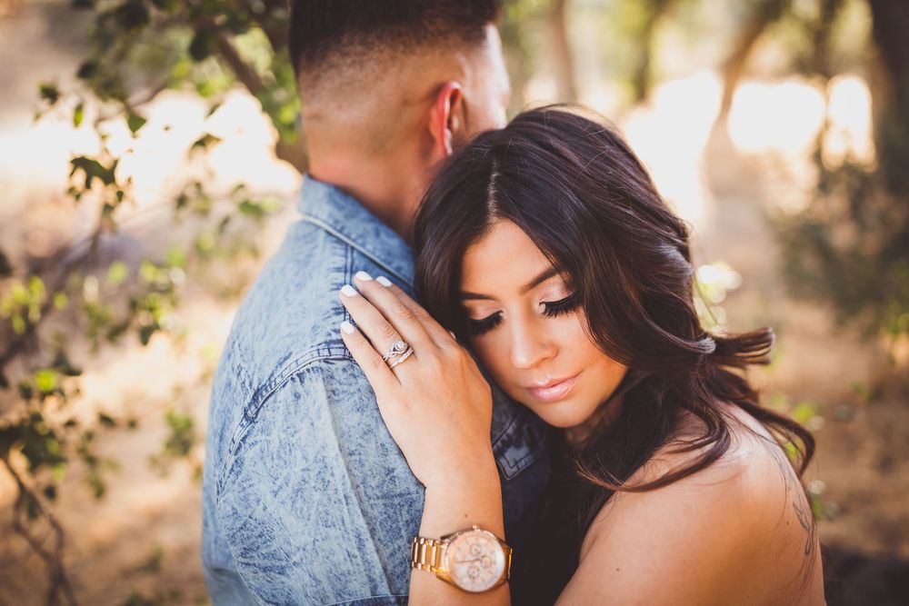 A couple embraces in a romantic outdoor photoshoot during golden hour with sunlit trees in the background.