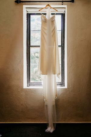 A white wedding dress hangs elegantly in front of a window, by Wollongong Wedding Photographer Serene Coleman