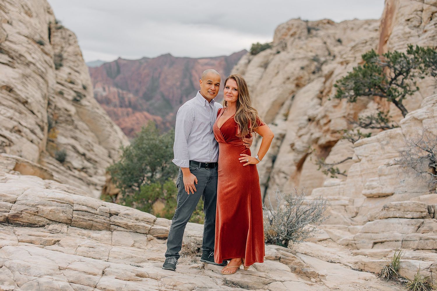 Desert landscape photoshoot with red dress against dramatic rock formations and mountain backdrop.