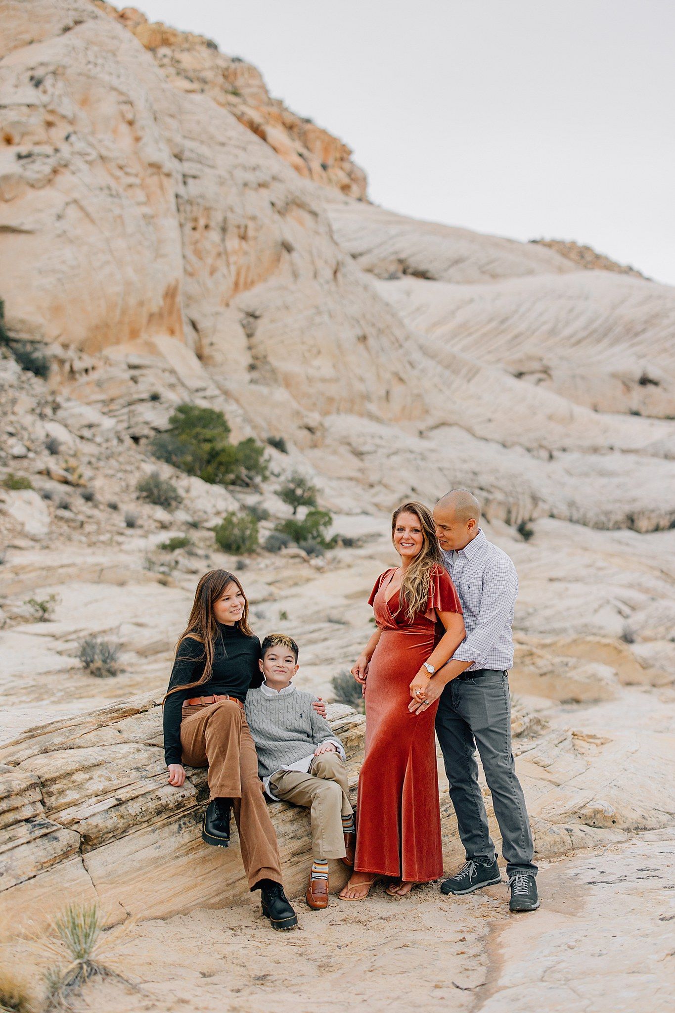 A family poses together on light-colored desert rock formations during an outdoor photo session.