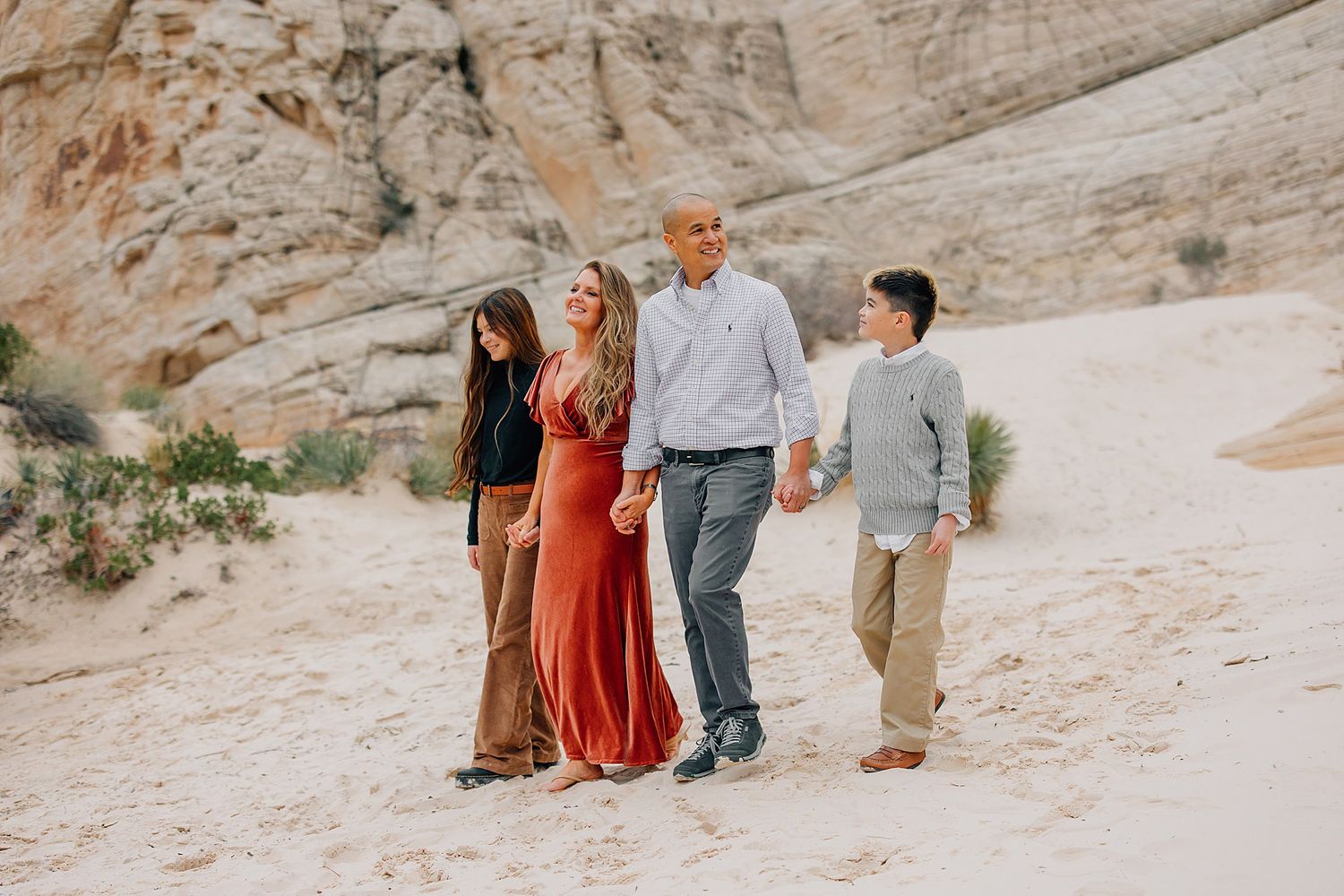 A family wearing coordinated earth-toned outfits walks together along a scenic desert rock formation path.