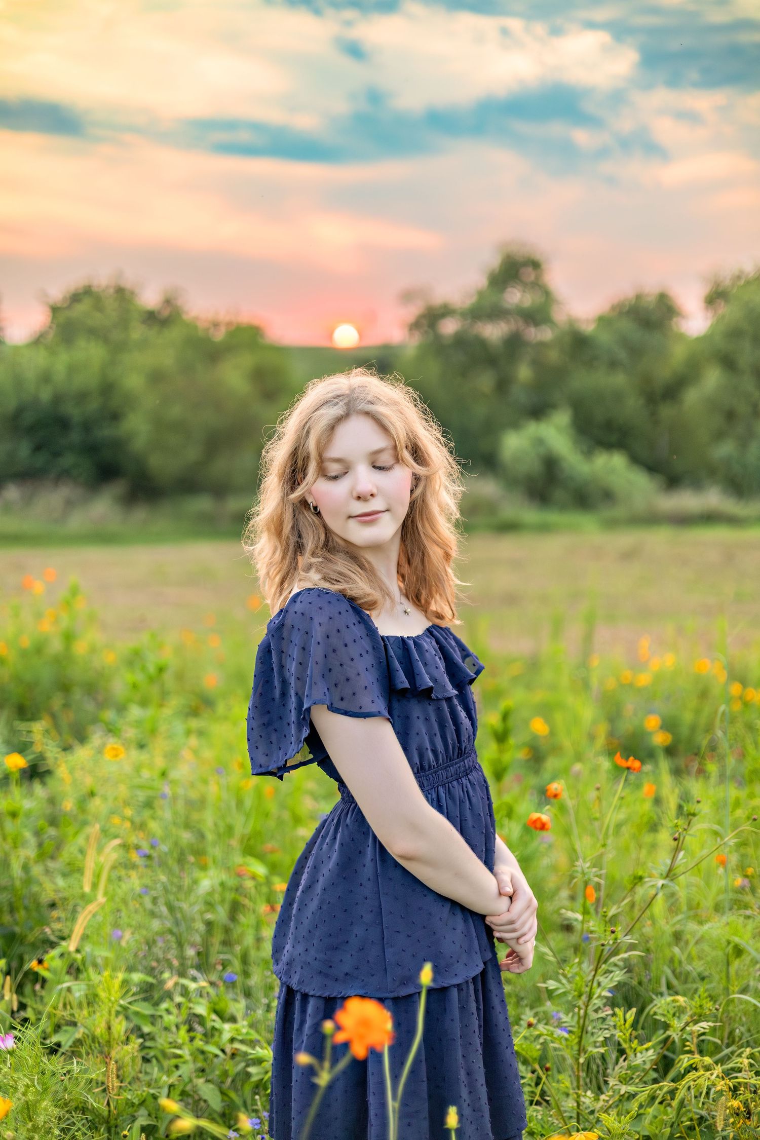 A dreamy summer scene shows someone in a navy blue dress twirling joyfully among vibrant wildflowers at sunset.