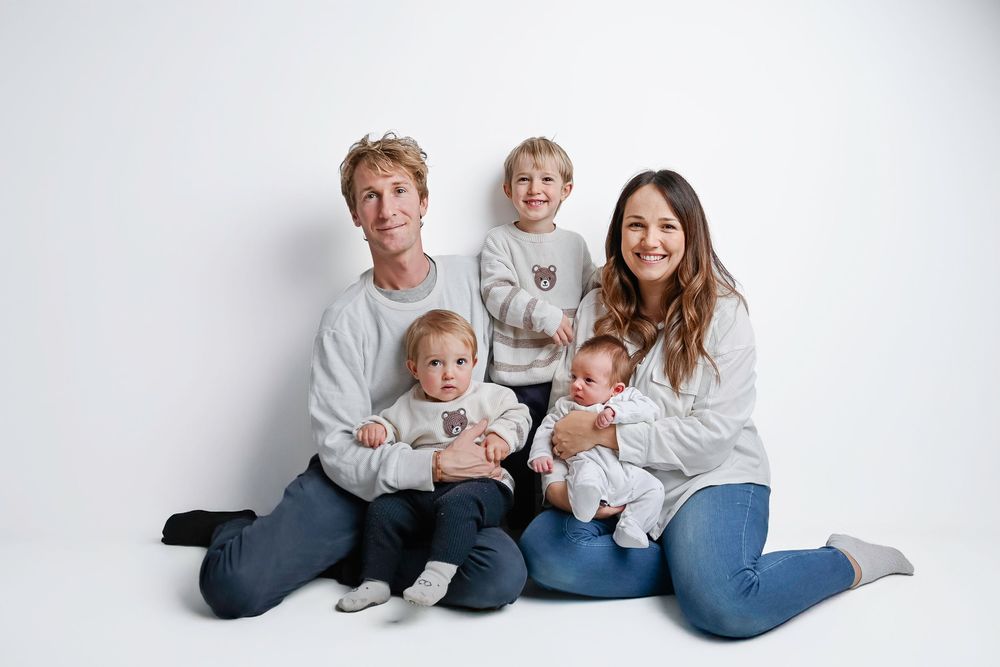 A family wearing coordinated white and denim outfits sits together on a white backdrop for a casual portrait session.