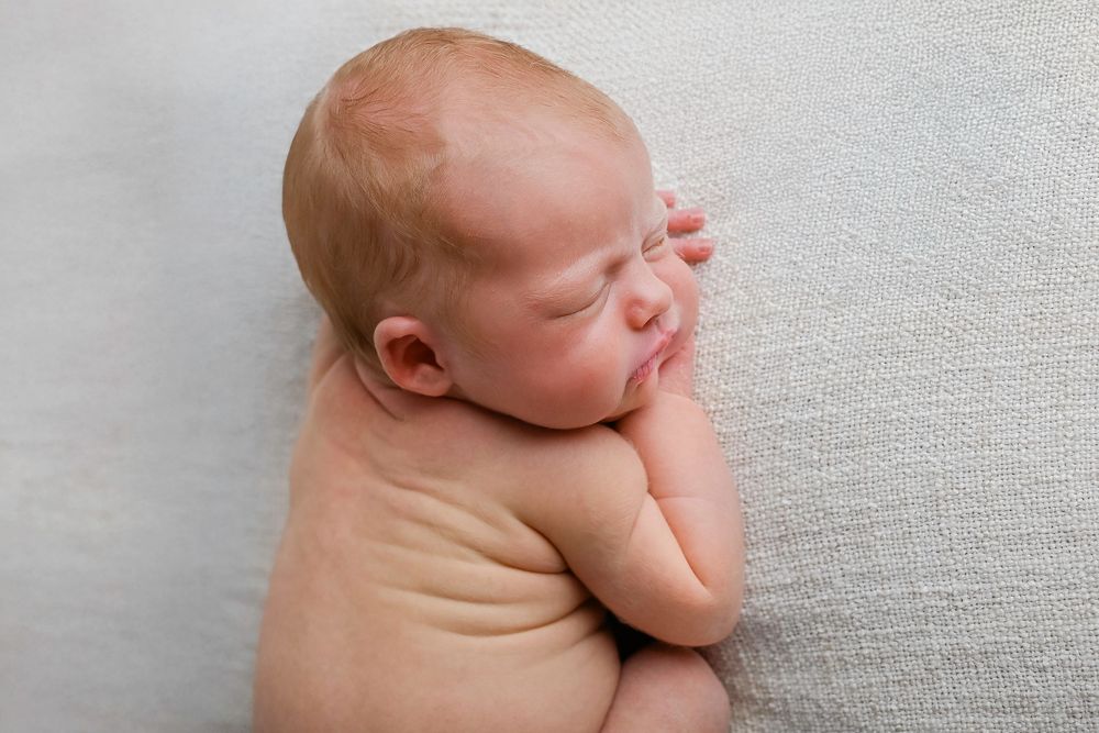 Sleeping newborn baby lying on soft gray fabric with peaceful expression and curled up position.