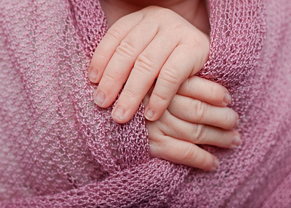 Close-up view of small baby hands against a soft pink knitted sweater texture.
