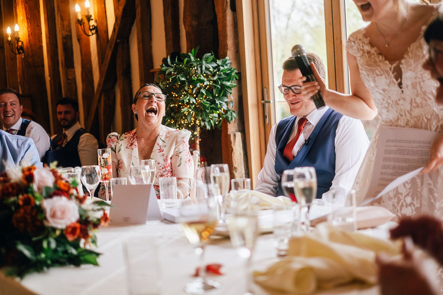 Crondon Park Wedding reception guests laughing and enjoying themselves at an elegant indoor venue with warm lighting and table settings.