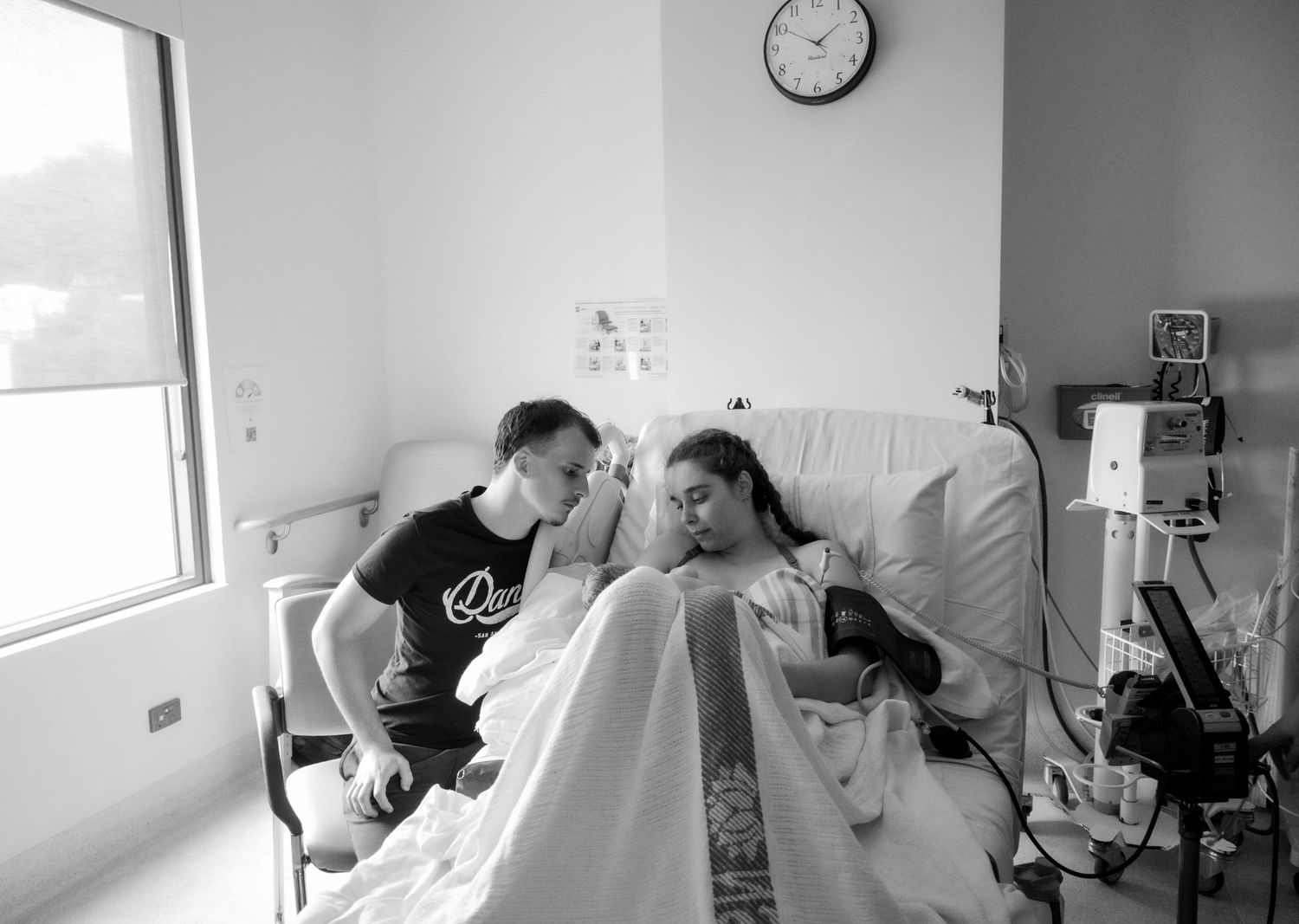 Black and white photo showing a tender moment between parents and newborn in a hospital room during a central coast birth photoshoot.