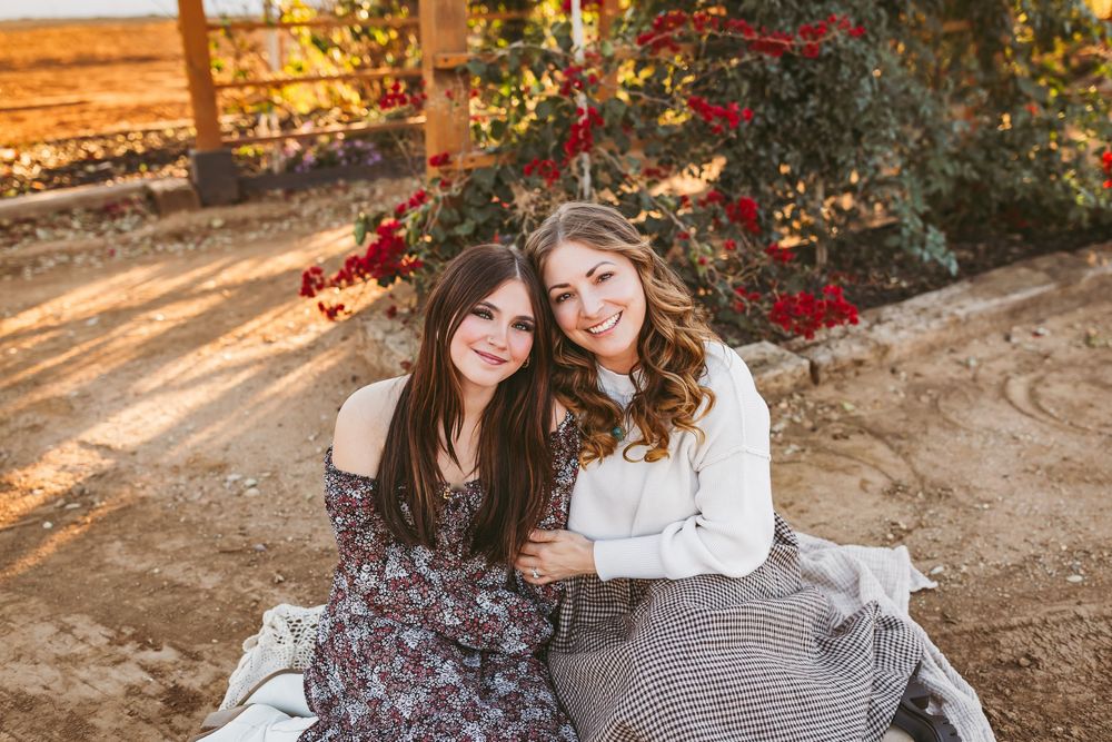 People sitting together outdoors during golden hour with red flowers and autumn foliage in the background.