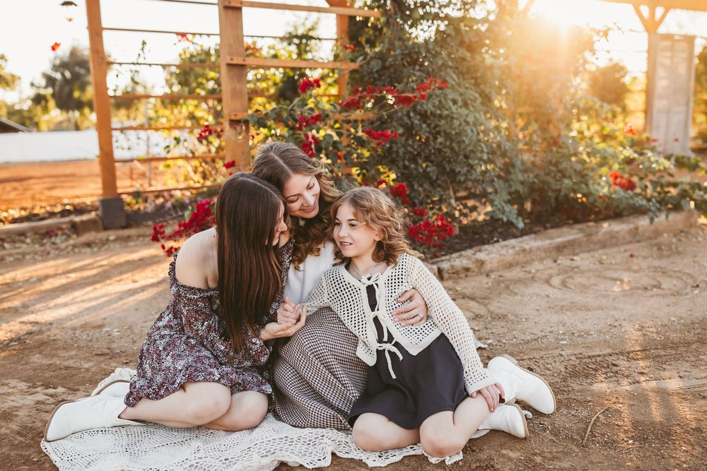 A couple sits together on the ground with their dog during golden hour sunset in a romantic outdoor setting.