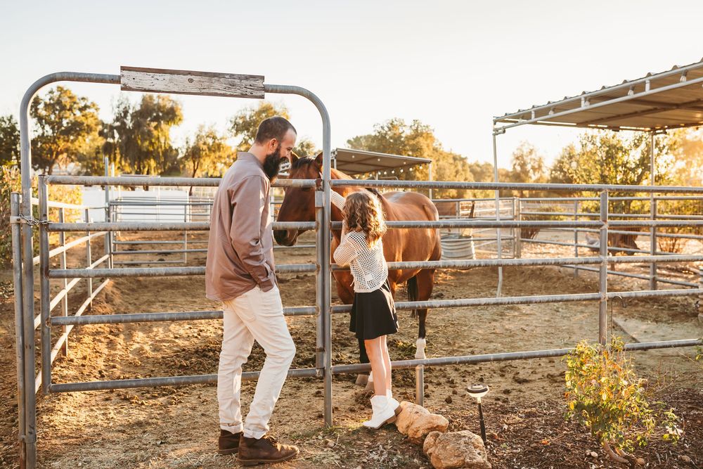 A group of people lean against a wooden fence at sunset in a rustic outdoor setting.